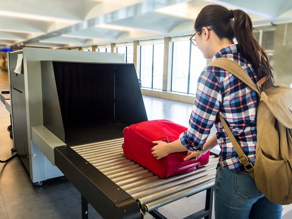 A photo of a woman placing her luggage on the conveyer belt for x-ray screening
