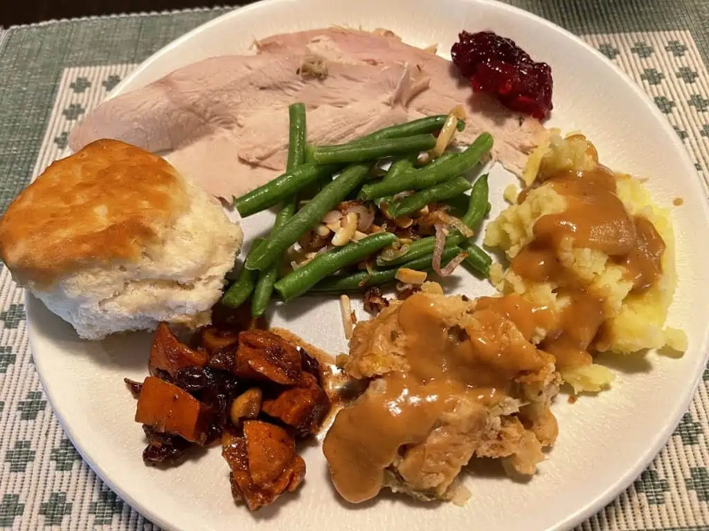 Traditional Thanksgiving Foods - A plate full of turkey, mashed potatoes, stuffing, candied sweet potatoes (yams) green beans and cranberry sauce