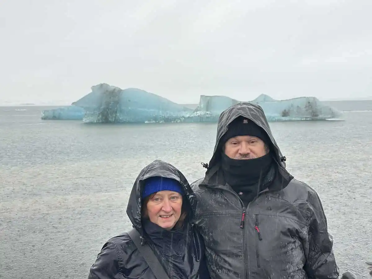The author and husband standing in the rain in front of a glacial iceberg at Glacier Lagoon in Iceland in January