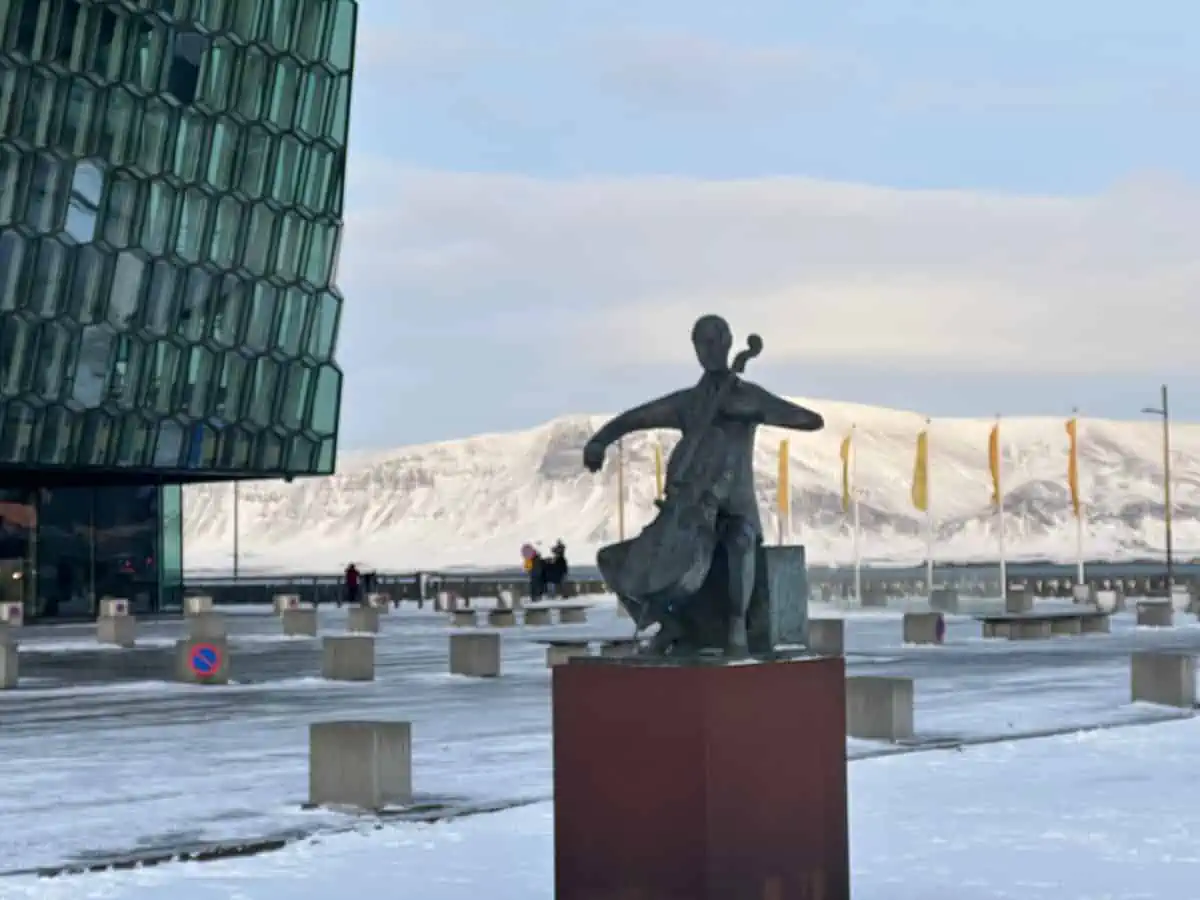 A statue of a cello player in front of the Harpa Music Center