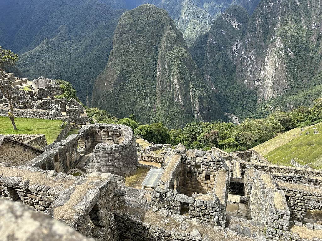 A view of Machu Picchu from a high trail, with the horseshoe shaped Temple of The Sun in the Middle of other stone ruins