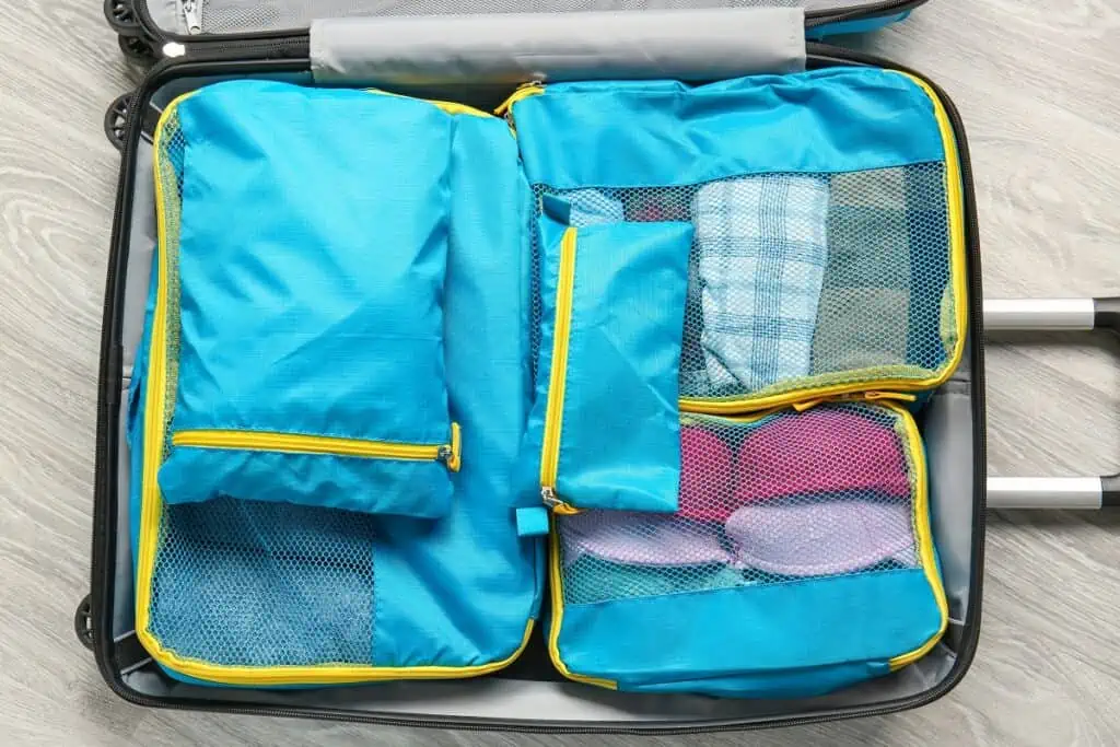 Suitcase and set of travel organizers with belongings on floor