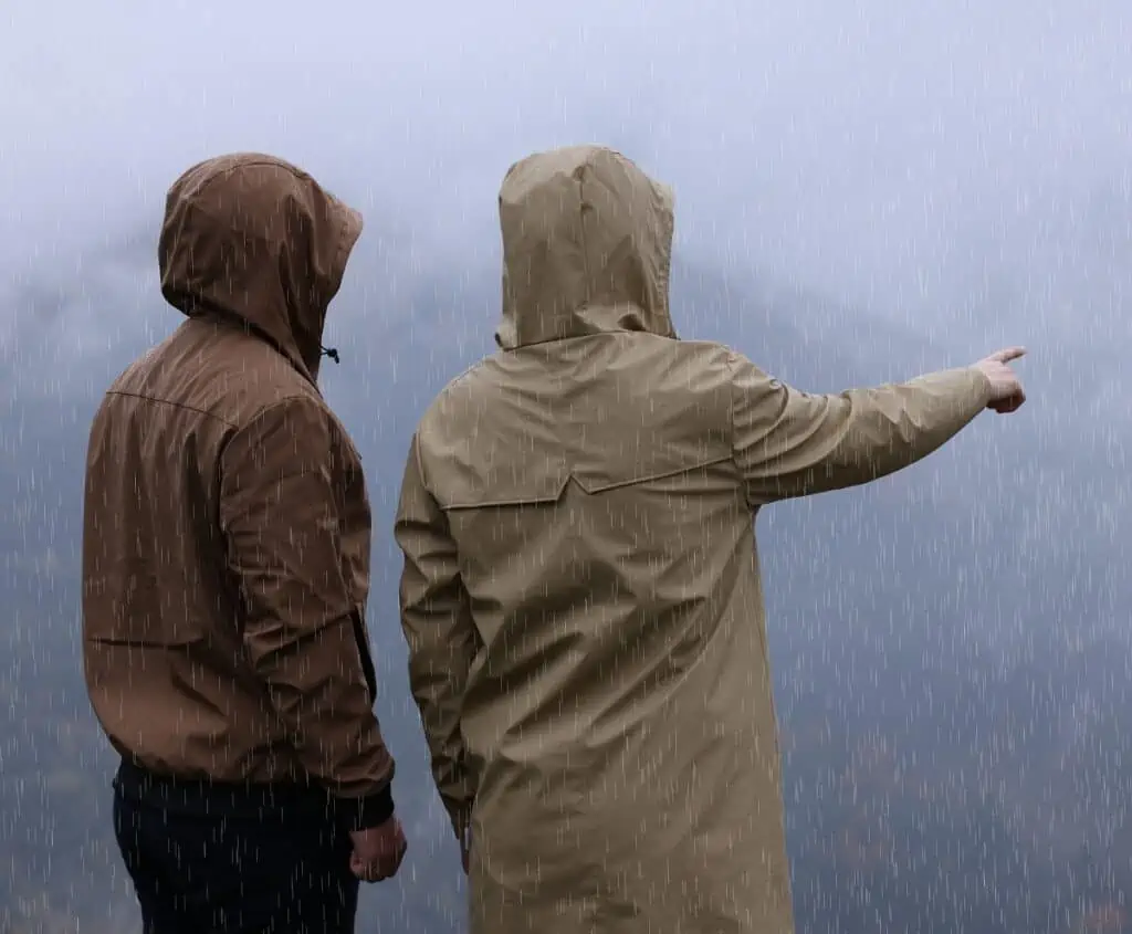 Man and woman in raincoats enjoying mountain landscape under rain