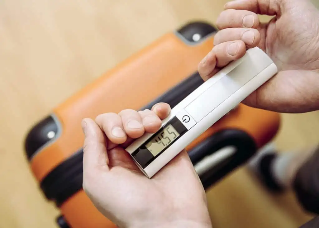 Person using a hand held luggage scale to weigh suitcase