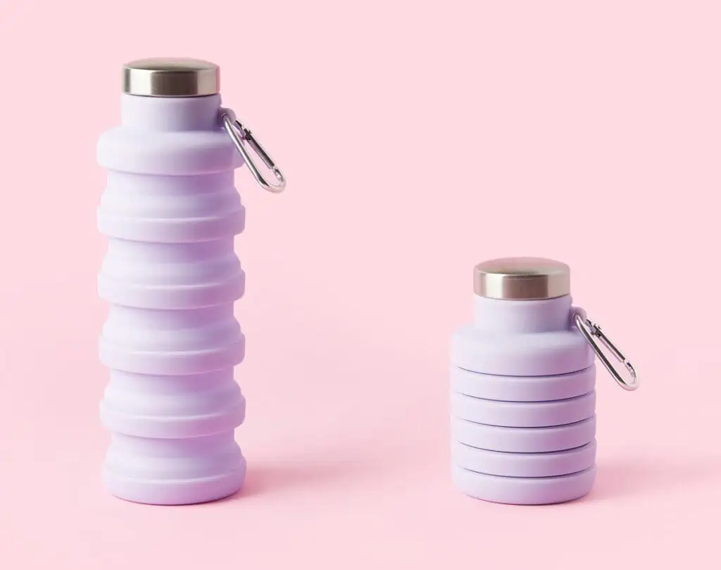 Collapsible reusable lilac water bottle on pink background. Sustainability, eco-friendly lifestyle