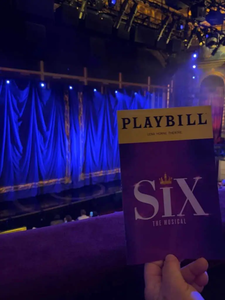 New York City Before A Cruise: Sailing From the Red Hook Cruise Terminal 11 a persons hand holding up the Playbill for Six with the stage in the background