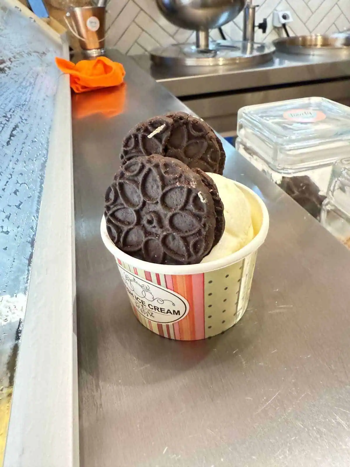 1 Day in Port: Exploring Rhodes Old Town on Foot – A Perfect Self-Guided Walk 15 Chocolate cookies with vanilla gelato served in a paper cup on a stainless steel counter at an ice cream shop.
