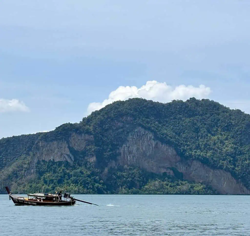 1 Day in Port: Phuket – A Private Phang Nga Bay Tour By Speedboat 15 Traditional longtail boat sailing on calm waters near lush green islands in Phang Nga Bay, Phuket, Thailand.