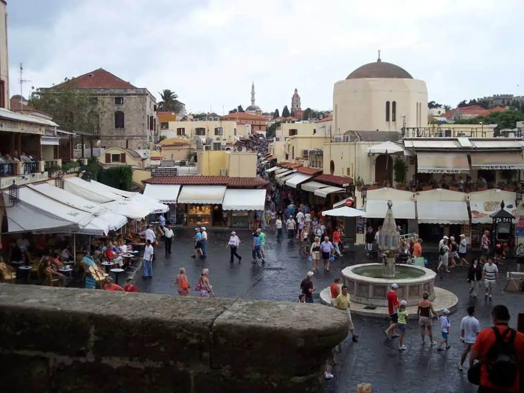 1 Day in Port: Exploring Rhodes Old Town on Foot – A Perfect Self-Guided Walk 1 Bustling main square in Rhodes Old Town with shops, cafes, and tourists enjoying a sunny day in Greece.